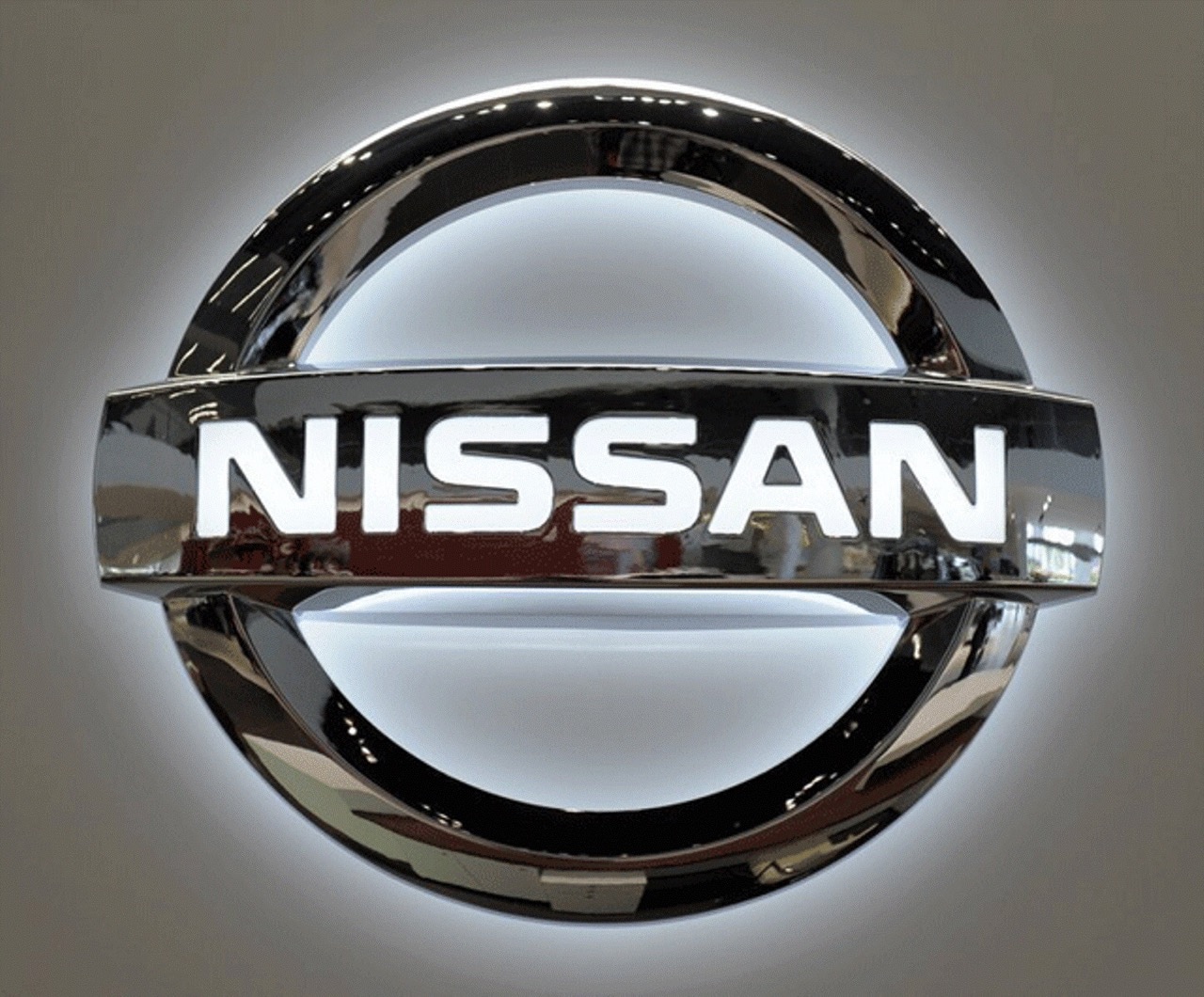 Metallic Nissan logo with white lettering on a chrome circular emblem, backlit with soft white glow
