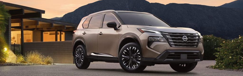 Bronze Nissan Rogue SUV parked outside a modern home with mountains in the background, showcasing its sleek design and bold front grille.