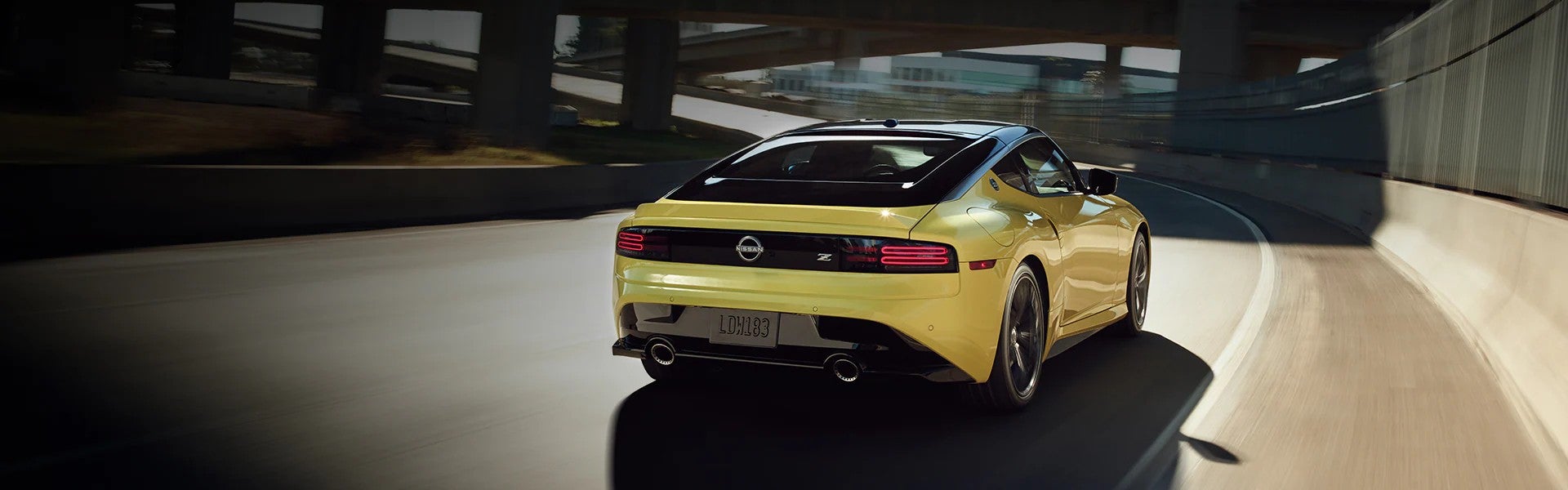 Yellow Nissan Z sports car driving on a curved road under an urban overpass.