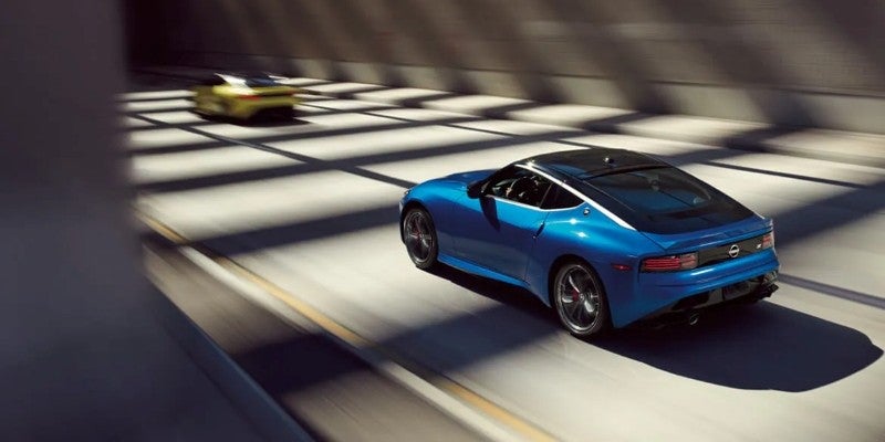 Blue Nissan Z sports car driving through a sunlit tunnel.
