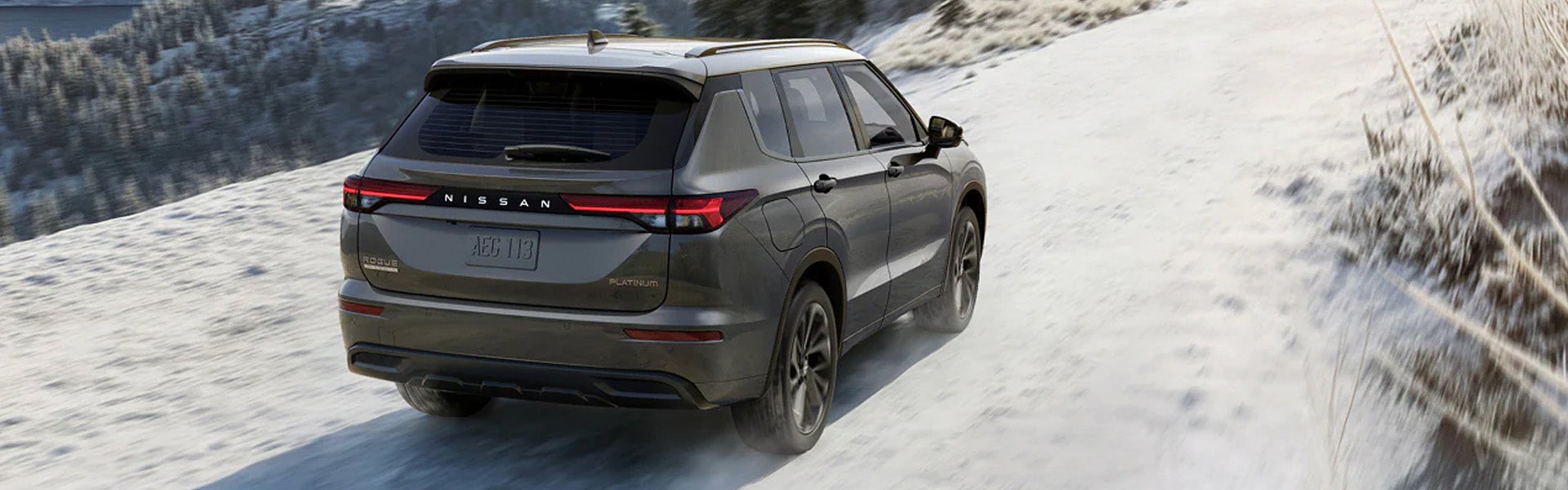 Gray Nissan Rogue Hybrid SUV driving on a snow-covered mountain road.