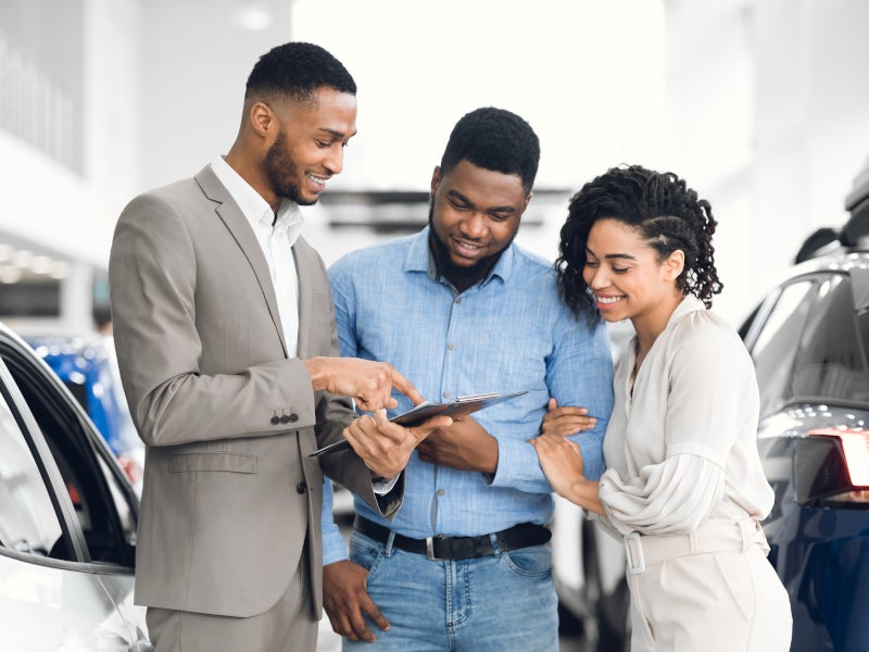 Salesperson showing car details in tablet to a young man and woman.