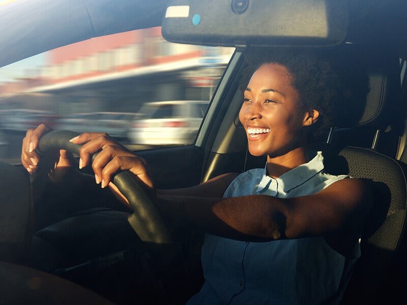 A woman is driving car with big smile on her face.