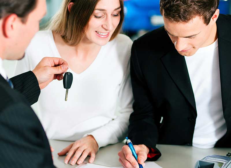 A man and woman sitting in front of a salesperson while the man signs a document.